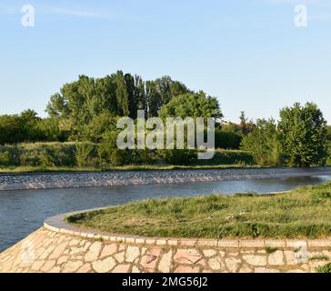 Beautiful nature in the City of Nis, Serbia, Europe. Quay on the Nisava River, trees, bushes, grass, stones and blue sky. Stock Photo