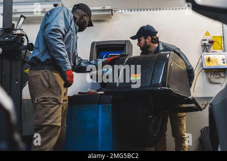 Low angle shot of black and white mechanics working by the computer in the repair shop. High quality photo Stock Photo