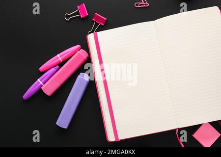 Blank open notebook, markers and binder clips on dark background Stock Photo