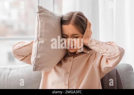 Irritated young woman with pillow suffering from loud noise at home, closeup Stock Photo