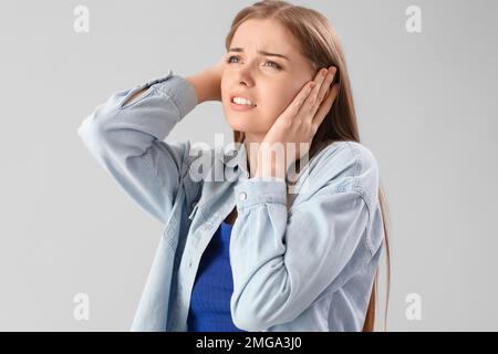 Young woman suffering from loud noise on grey background, closeup Stock Photo