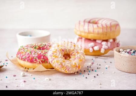 Parchments with different delicious donuts and bowls of sprinkles on white table Stock Photo