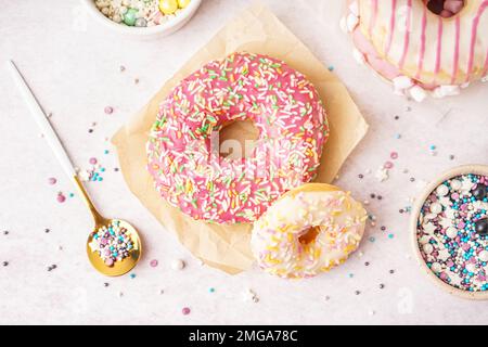 Parchments with different delicious donuts and bowls of sprinkles on white table Stock Photo