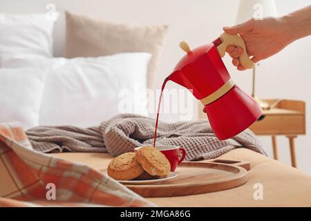 Woman pouring espresso from geyser coffee maker into cup on bed Stock Photo