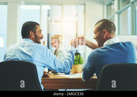 Making it to the top of their game. Rear view shot of two businessmen fist pumping in an office. Stock Photo
