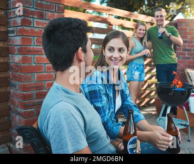 Friends (for now). a young man and woman chatting and having beers at a barbecue with friends. Stock Photo