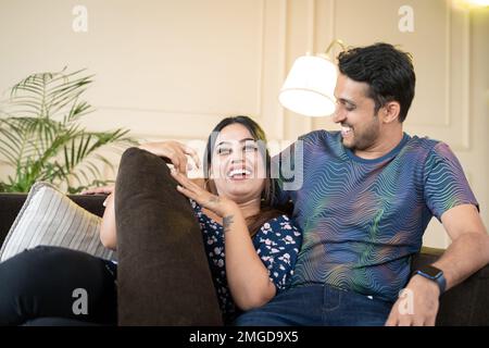 Happy laughing couple spending some good family time at home while on couch by talking eachother - concept of romantic, dating and family lifestyle Stock Photo