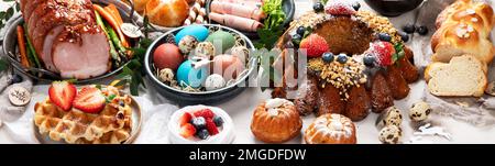 Traditional Easter dinner or  brunch with ham, colored eggs, hot cross buns, cake and vegetables. Easter meal dishes with holday decorations. Panorama Stock Photo