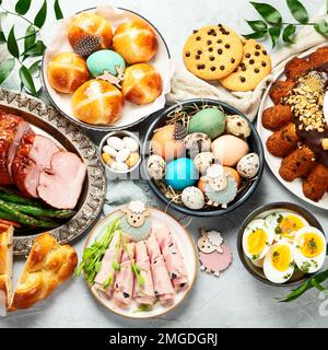 Classic Easter ham dinner. Top view table scene on a white background. Ham, eggs, hot cross buns, carrot, cake and vegetables. Stock Photo
