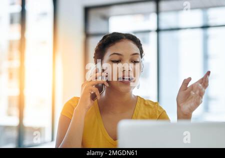 Im looking at the files as we speak...a young designer talking on a cellphone while working on a laptop in an office. Stock Photo