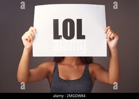 That deserves a lol. Studio shot of a young woman holding a sign with lol printed on it against a gray background. Stock Photo