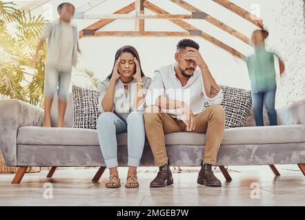 Tired parents, running children and family in a room feeling anxiety, headache and stress. Kids chaos, sofa jump and fatigue of mom and father Stock Photo