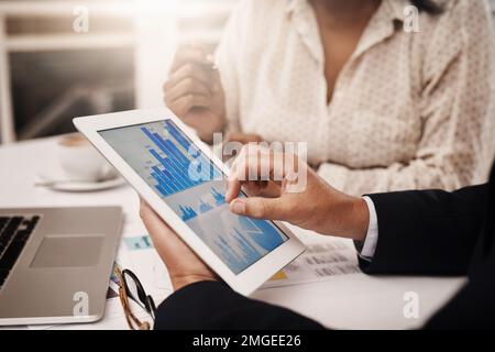 Taking a detailed look at their business stats. Closeup shot of two unrecognisable businesspeople analysing graphs on a digital tablet in an office. Stock Photo