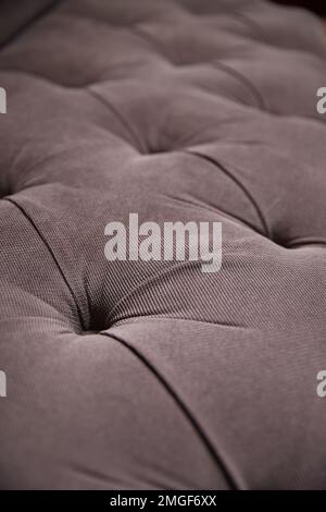 Grey upholstery of a very soft sofa with buttons made of thick fabric. Close-up Stock Photo