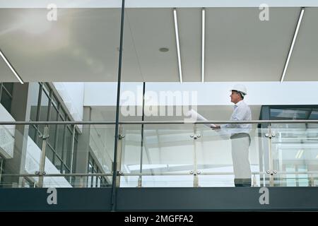 Supervisor on site. a focused professional male architect looking at a development site while holding blueprints inside a building. Stock Photo
