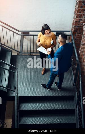 Collaborating to gain a big leads in the industry. two designers having a discussion on a staircase in an office. Stock Photo