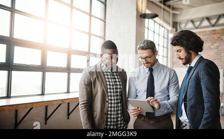 Three heads are always better than one. three well-dressed businessmen brainstorming together over a tablet in their office. Stock Photo