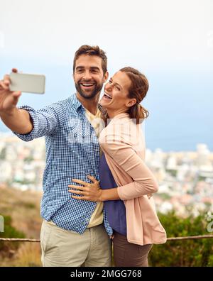 We just cant resist a selfie moment. an affectionate couple taking selfies outside. Stock Photo