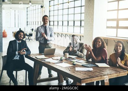 You deserve some applause, too. Portrait of a group of businesspeople applauding while sitting around a boardroom table in the office. Stock Photo