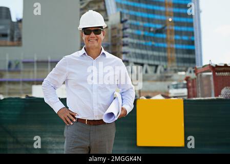 This is the most exciting project Ive worked on yet. Portrait of a professional male architect standing on a building site while holding blueprints Stock Photo