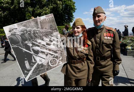 People dressed in Soviet army uniform, wearing face masks to protect against coronavirus, hold a poster depicting a photo of the 1945 Victory Parade in Moscow at a memorial to World War II veterans in a memorial park in Kyiv, Ukraine, Saturday, May 9, 2020 on the 75th anniversary of the end of World War II. Ukraine marks the 75th anniversary of the end of World War II in Europe at a time of coronavirus lockdown and loneliness spent in search of memories both bitter and sweet. (AP Photo/Efrem Lukatsky)