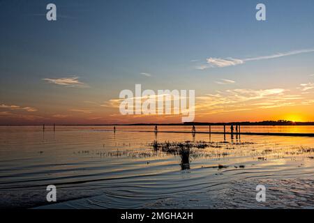Ares (south-western France): sunset over the Arcachon Bay. Silhouettes of walkers and cyclists by the pier covered by the sea at high tide and wooden Stock Photo