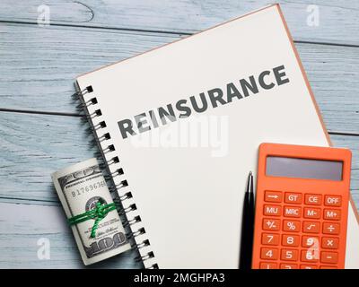 Top view image text reinsurance on the notebook with a pen, calculator and money on the table. Stock Photo