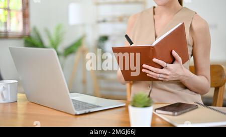 cropped image, Beautiful millennial Asian businesswoman or female boss working at her desk, taking notes or making lists on her notebook. Stock Photo
