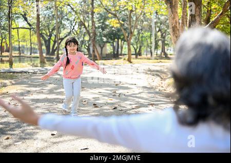 An adorable Asian little girl, granddaughter running to her grandmother, playing fun game in the park together. family bonding activity concept Stock Photo