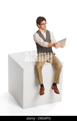 Young thoughtful business man wearing modern office style clothes sitting and using digital tablet isolated on white background. Business, work Stock Photo