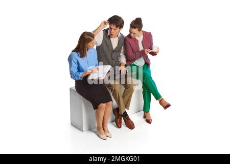 Emotional young people, businessmen, co-workers sitting and discuss new project terms isolated over white background. Teamwork, business process Stock Photo