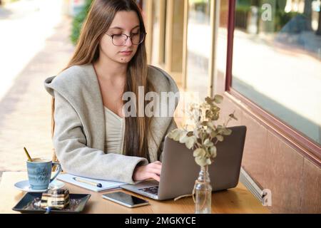 Business woman working remotely on a laptop in a coffee shop. Stock Photo