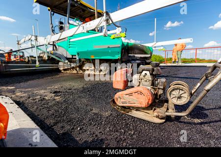 View on worker who is compacting asphalt with vibration plate, compactor machine on the bridge under construction. Stock Photo