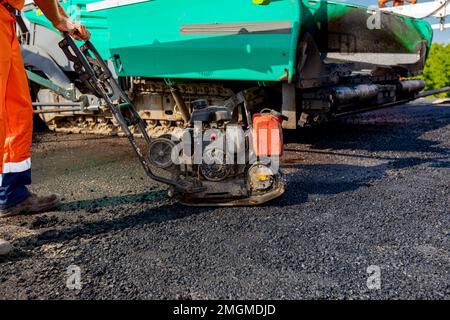 View on worker who is compacting asphalt with vibration plate, compactor machine on the bridge under construction. Stock Photo