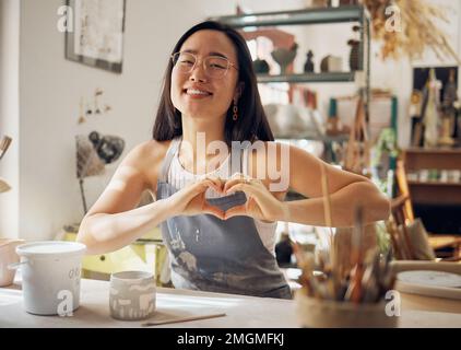 Happy woman, portrait or heart hand gesture in pottery studio, Asian small business or creative ceramic workshop. Smile, clay or art mud worker in Stock Photo
