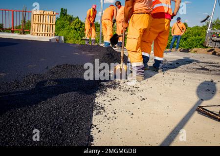 Few workers are using shovels to level, set up layer of fresh tarmac to right measures, pouring hot asphalt. Stock Photo