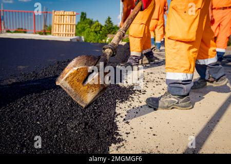 Few workers are using shovels to level, set up layer of fresh tarmac to right measures, pouring hot asphalt. Stock Photo