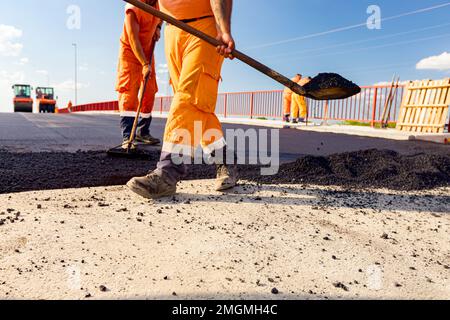 Few workers are using shovels to level, set up layer of fresh tarmac to right measures, pouring hot asphalt. Stock Photo