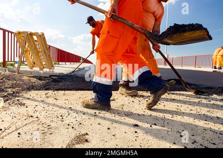 Few workers are using shovels to level, set up layer of fresh tarmac to right measures, pouring hot asphalt. Stock Photo