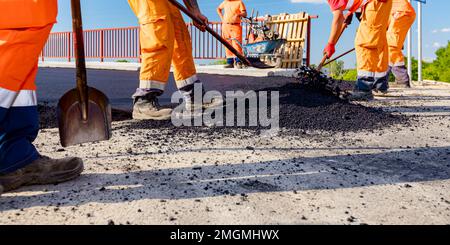 Few workers are using shovels to level, set up layer of fresh tarmac to right measures, pouring hot asphalt. Stock Photo