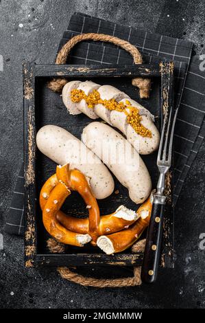 Bavarian meal with white sausages and sweet mustard in wooden tray with Pretzel. Black background. Top view. Stock Photo