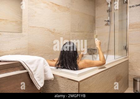 A beautiful brunette enjoys an evening alone in the bathtub with a glass of champagne. Stock Photo