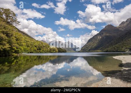 A man fishing from the banks of the calm waters of Lake Gunn in the South Island of New Zealand with David Peaks in the distance Stock Photo