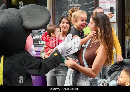 Tenerife, Spain - January 26, 2023: Middle-aged woman with a little girl in her arms smiling while an actor dressed as Mickey Mouse gestures with his Stock Photo