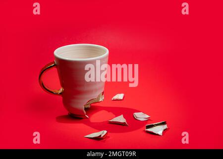Broken tea cup isolated on red background. Cracked coffee mug and fragile ceramic pieces Stock Photo