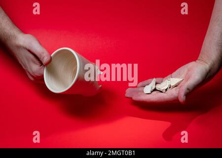 Man holding broken tea cup isolated on red background. Close up of arm holding cracked coffee mug Stock Photo