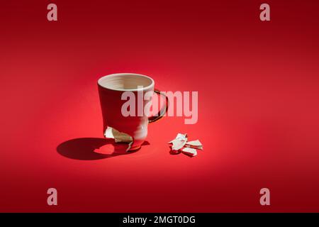Broken tea cup isolated on red background. Cracked coffee mug and fragile ceramic pieces Stock Photo