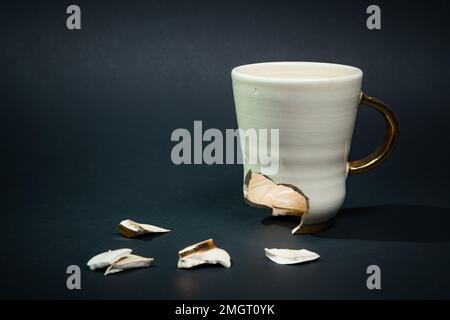 Broken tea cup isolated on black background. Cracked coffee mug and fragile ceramic pieces Stock Photo