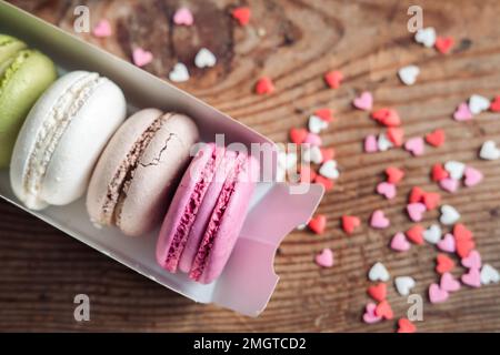 Assorted macarons in a box sprinkled with small hearts on a wooden background, top view Stock Photo