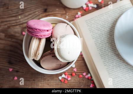 Macaroons in a bowl, a cup of coffee, on a background of small hearts on a wooden background Stock Photo